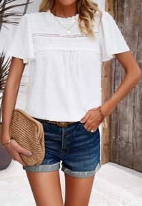Detail of white short sleeve top featuring lace trim, smocked chest, and Swiss dot texture