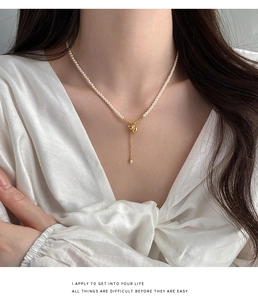 Détail du collier de perles avec pendentif gourde dorée et pompon sur soie