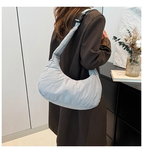 Back view of a light blue puffy crescent shoulder bag worn on the shoulder by a model