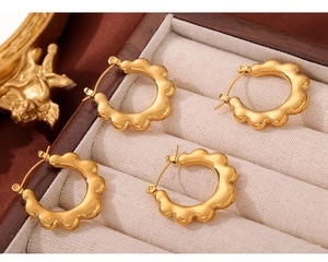 Close-up of four gold-plated wave-edged hoop earrings displayed on a vintage jewelry box