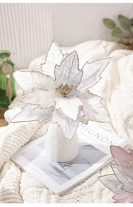 Macro detail of artificial white poinsettia with silver glitter on a white knit blanket