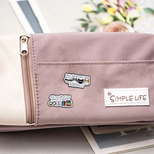 Detailed macro view of beige canvas pencil case with cute enamel pins and woven logo tag