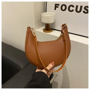 Brown PU leather crescent shoulder bag with gold hardware held in a modern interior