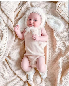 Detail of infant beige ribbed bodysuit with rabbit ear hat and lace socks on soft fabric