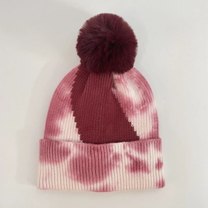 Close-up of pink and burgundy tie-dye knit beanie with fluffy faux fur pompom detail