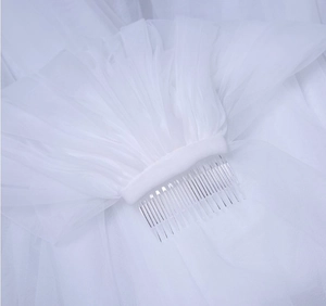 Close-up of white bridal veil featuring a clear plastic hair comb and gathered tulle detail