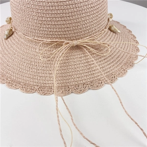 Detail of pink straw hat featuring a scalloped edge and decorative shell pendant