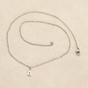 Macro shot of silver stainless steel chain with a minimalist letter A pendant on beige surface