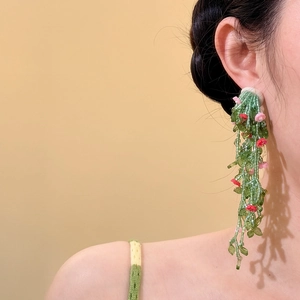 Detailed view of handmade green beaded tassel earrings with floral accents on model.