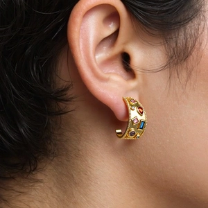 Detailed view of C-shaped gold hoop earrings with colorful inlaid gemstones on ear