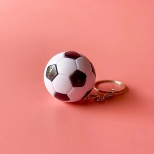 Détail d'un mini porte-clés de football noir et blanc avec anneau sur fond rose doux
