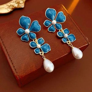 Macro shot of blue enamel flower earrings with gold plating and teardrop pearl charms