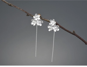 Detailed view of matte silver flower earrings hanging on a natural wooden branch