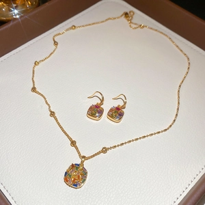 Close-up of gold plated jewelry set with colorful square zircon stones on white texture