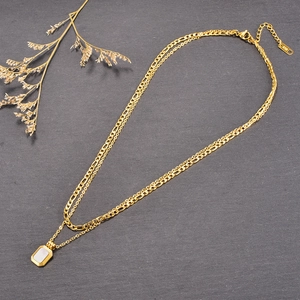 Detail of double-layer gold necklace with rectangular white pendant on stone texture