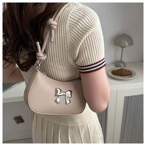 Detail of the chic beige shoulder bag featuring a silver metal bow and knotted strap design