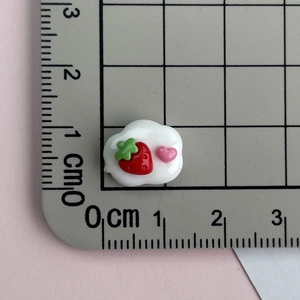 Close-up of a pink resin cloud accessory with strawberry detail showing dimensions on a ruler