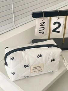 Close-up of quilted cream makeup bag with black bow prints and fabric label detail