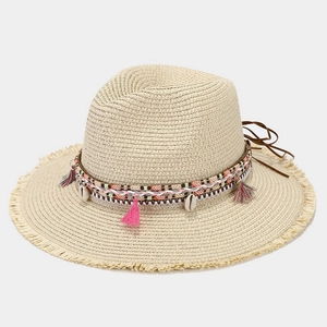 Détail d'un chapeau de paille beige avec pompons bohèmes et coquillages naturels
