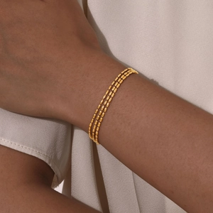 Detailed view of layered 18K gold-plated beaded triple-strand bracelet on a model's wrist