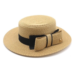 Detail of khaki straw hat with a large bow and gold letter M metal ornament