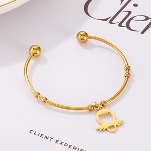 Detail of golden open bangle featuring a hollow heart wing charm and ball ends