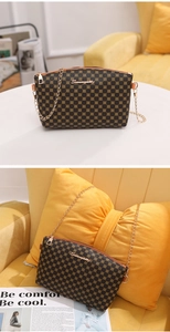 Detail of a brown printed crossbody bag for women with gold chain and logo on a sofa