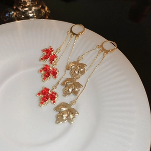Détail de boucles d'oreilles feuilles d'érable dorées avec strass rouges sur plat blanc