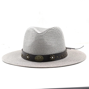 Detail of light gray straw fedora hat featuring a brown leather band and gold sun studs