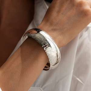 Detail of silver snake scale textured wide cuff bracelet worn on female wrist