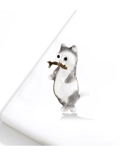 Macro view of grey and white enamel cat brooch with a golden fish in its mouth