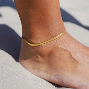 Classic golden herringbone snake chain anklet worn on beach with bright natural lighting