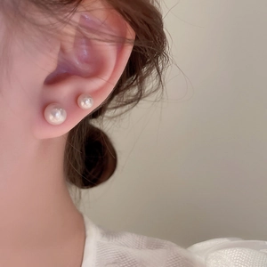 Close-up detail of elegant white pearl stud earrings on model for a layered jewelry look