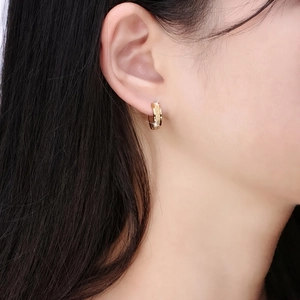 Close-up of golden stainless steel hoop earrings with sparkling frosted texture on ear lobe