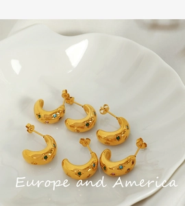 Macro view of gold-plated C-shape hoop earrings with colorful zircon stones in a tray