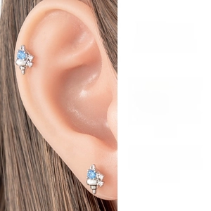 Close-up of blue zircon conch ear studs worn on ear cartilage with a silver metal finish