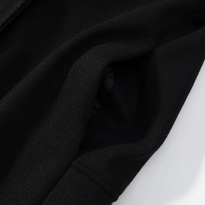 Detailed close-up of pocket stitching and heavy wool texture on black long coat