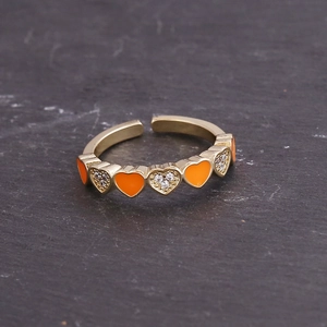 Macro shot of gold-plated open ring with orange enamel hearts and white zircon settings
