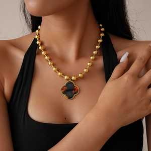 Detail view of a gold beaded necklace featuring a large tortoise shell clover pendant on a model