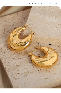 Detailed close-up of gold-plated crescent hoop earrings with hammered relief texture