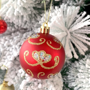 Dettaglio pallina di Natale rossa opaca con glitter dorati su rami innevati di bianco