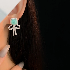 Macro shot of silver bow earrings featuring a rectangular green zircon and fine crystals