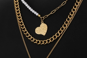 Detail of layered gold link chain and white pearl necklace with hammered heart pendant
