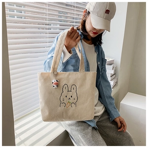 Detail of beige corduroy tote bag with rabbit embroidery held by model in casual setting