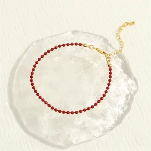 Detail of red beaded bracelet with golden adjustable lobster clasp on glass tray