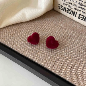Macro shot of deep wine red flocked heart earrings on a vintage beige linen surface