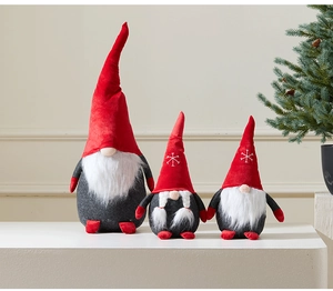 Three plush red and grey Christmas gnomes with snowflake embroidery on a white display stand