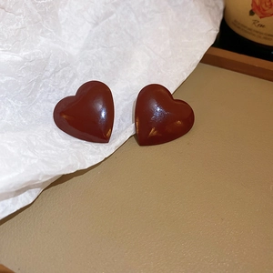 Close-up of glossy burgundy heart-shaped earrings on textured surface with soft lighting