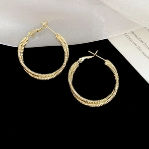 Close-up of golden textured hoop earrings with multi-layered design on black velvet