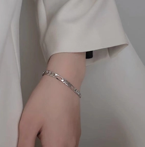 Close-up of a silver Figaro chain bracelet on a model's wrist with polished finish